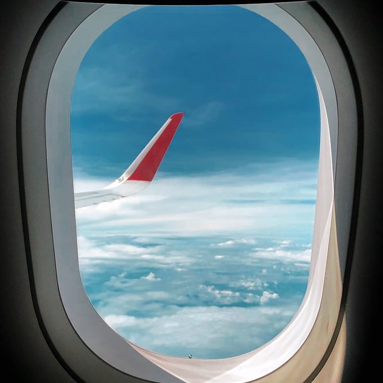 Comparateur de vols Vue depuis un hublot d'avion, montrant un aile et un ciel nuageux.